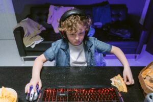 A focused young gamer engages in a nighttime gaming session with snacks and a headset.